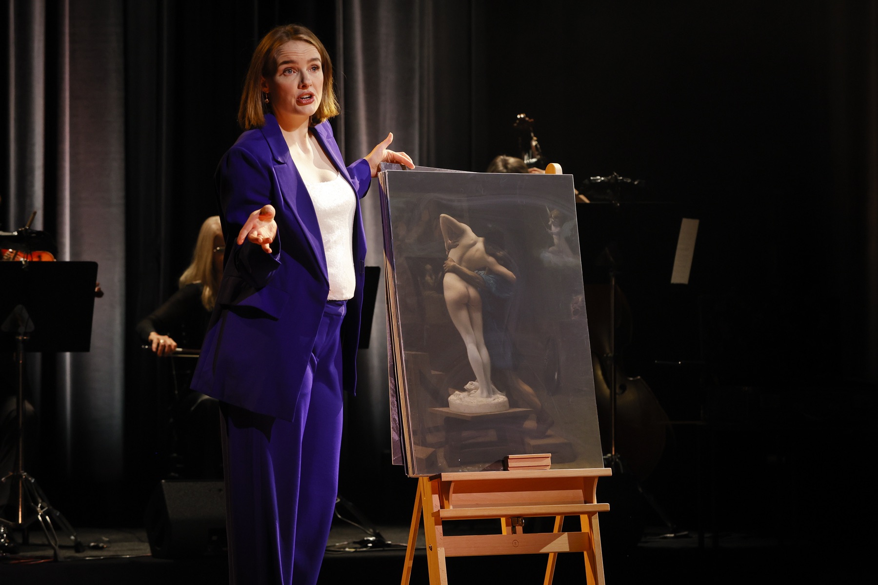 Anna O'Byrne on stage beside a portrait of Eliza Doolittle in Becoming Eliza